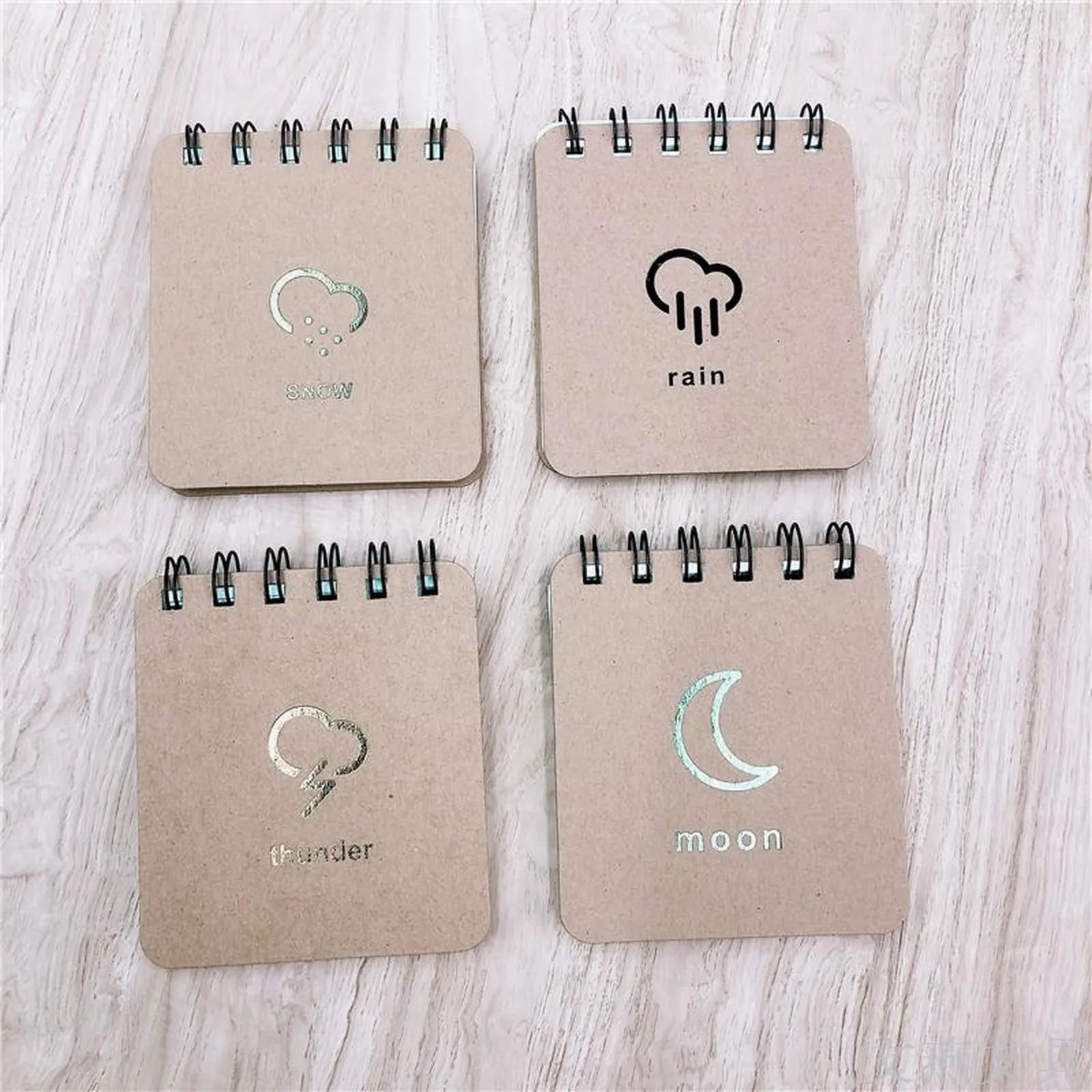 Four mini kraft spiral notebooks with snow, rain, thunder and moon icons