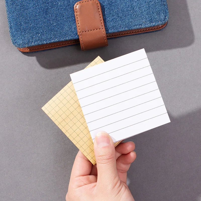 Hand holding a white lined and a kraft grid sticky note