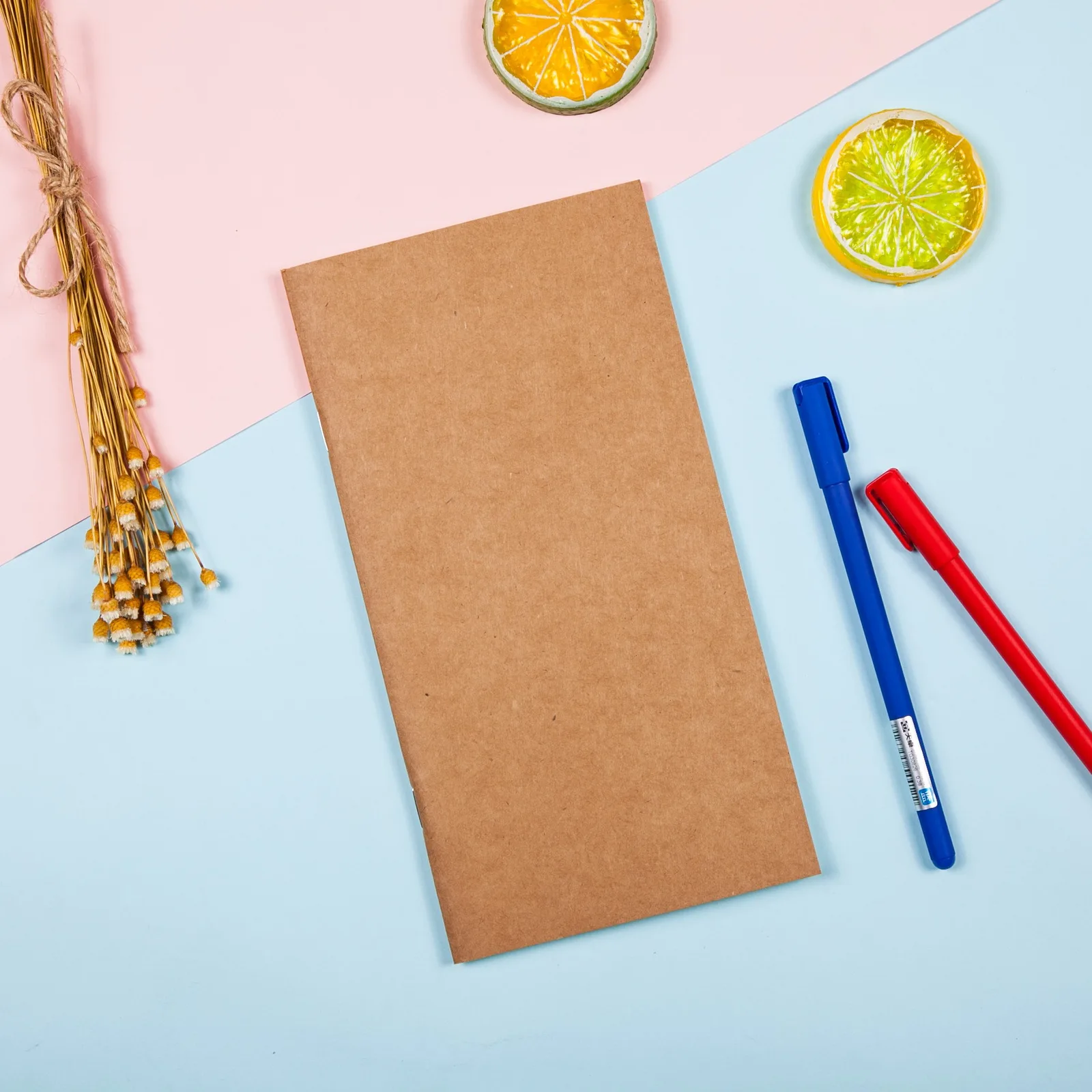Kraft pocket notebook on a pink and blue desk with pens